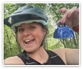 Alesia Smith wearing a bike helmet and biking clothes, smiling and holding a bell to cheer on riders